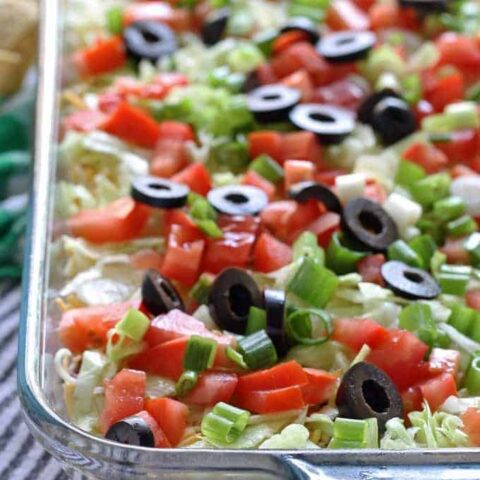 Go big with this 8 layer taco dip recipe - it is the perfect appetizer for large crowds. It's full of meat, cheese, veggies and more! | honeyandbirch.com