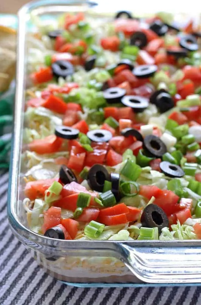 Go big with this 8 layer taco dip recipe - it is the perfect appetizer for large crowds. It's full of meat, cheese, veggies and more! | honeyandbirch.com