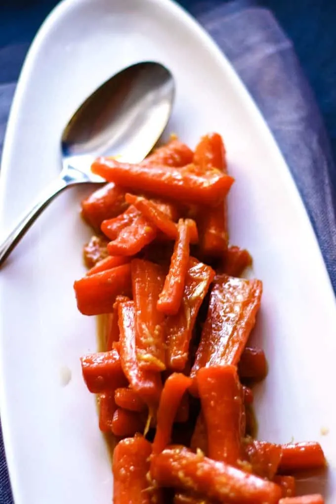 ginger candied carrot recipe on a white serving plate with a serving spoon