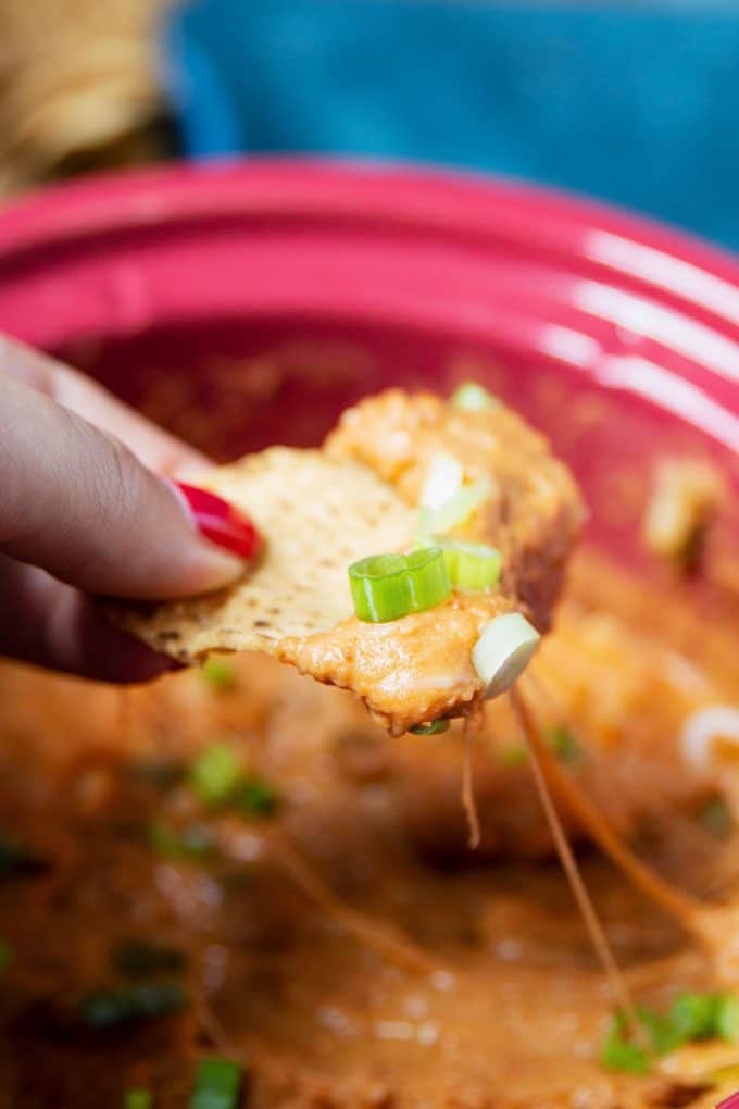 a tortilla chip with slow cooker bean dip. Melted cheddar cheese can be seen coming from the crock pot to the chip.