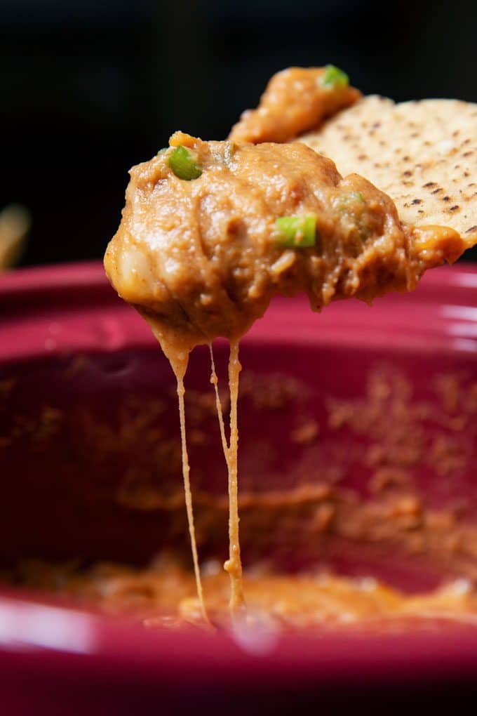 a crock pot bean dip cheese pull picture, with the dip topped with green onions