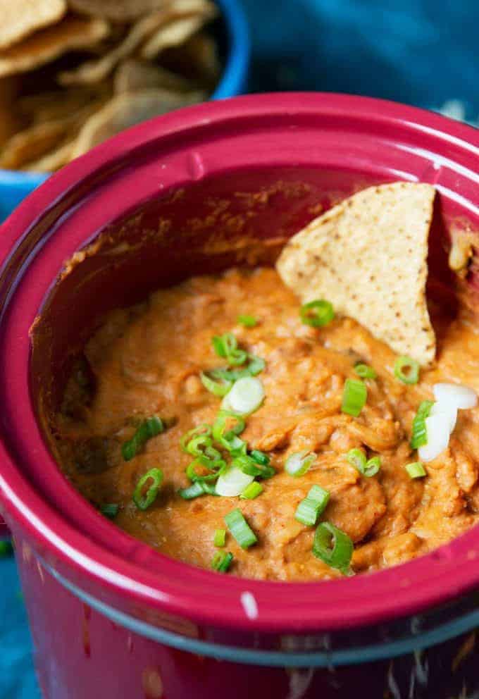 a red slow cooker filled with crock pot bean dip with a chip
