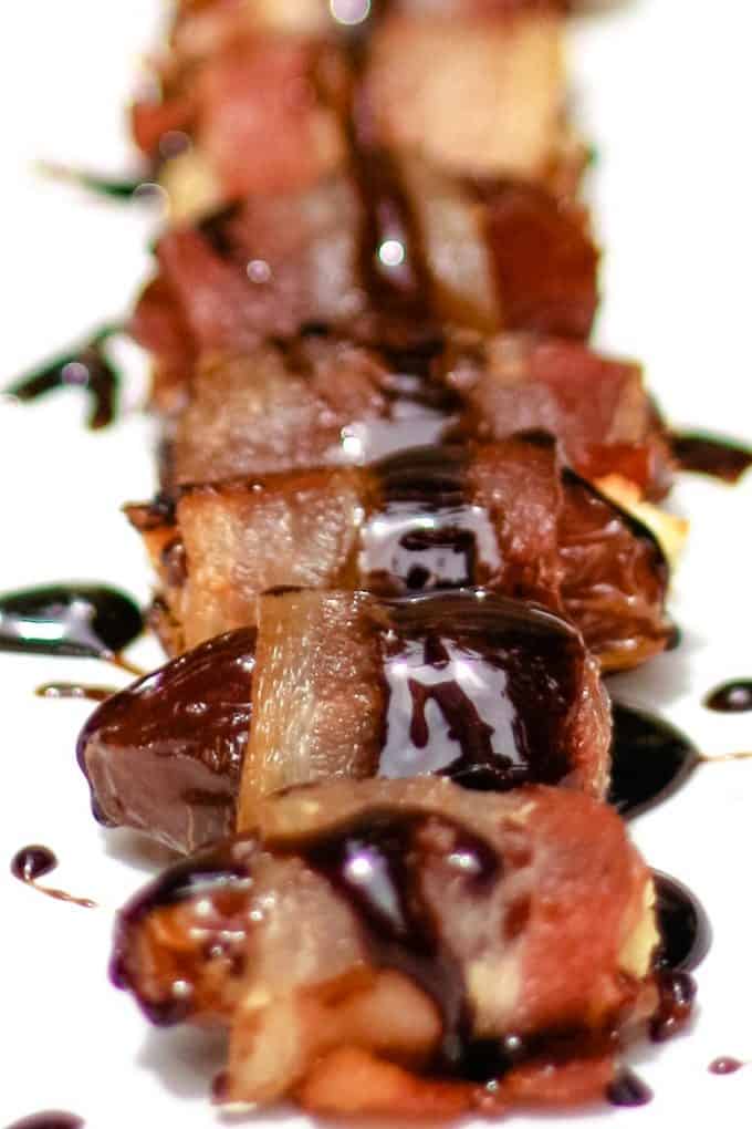 bacon wrapped dates on a white plate