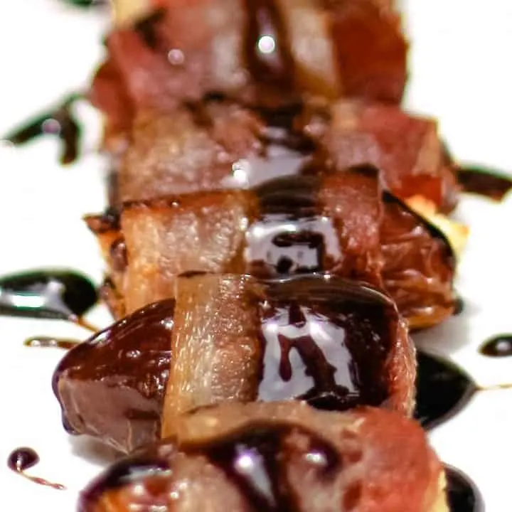 bacon wrapped dates on a white plate