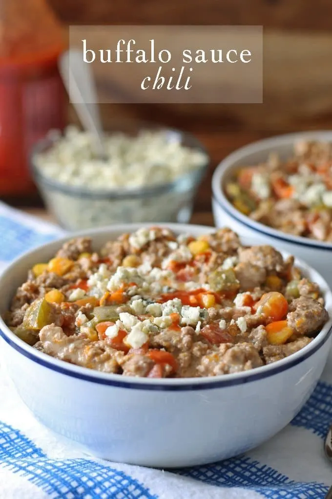 bowl of buffalo sauce chili on a blue napkin with blue cheese crumbles in a small bowl
