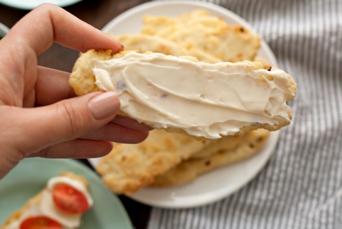 hand holding a flatbread cracker covered in soft cheese