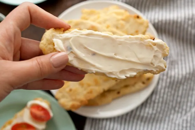 hand holding a flatbread cracker covered in soft cheese