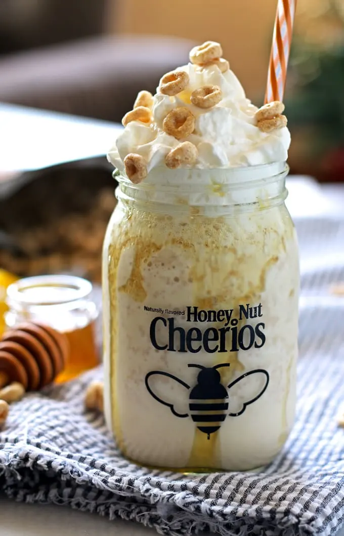 honey nut Cheerios mug filled with cereal milkshake topped with whipped cream, Honey Nut Cheerios. orange striped straw
