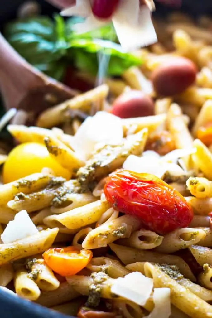 shaved parmesan being sprinkled over pasta with tomatoes and pesto