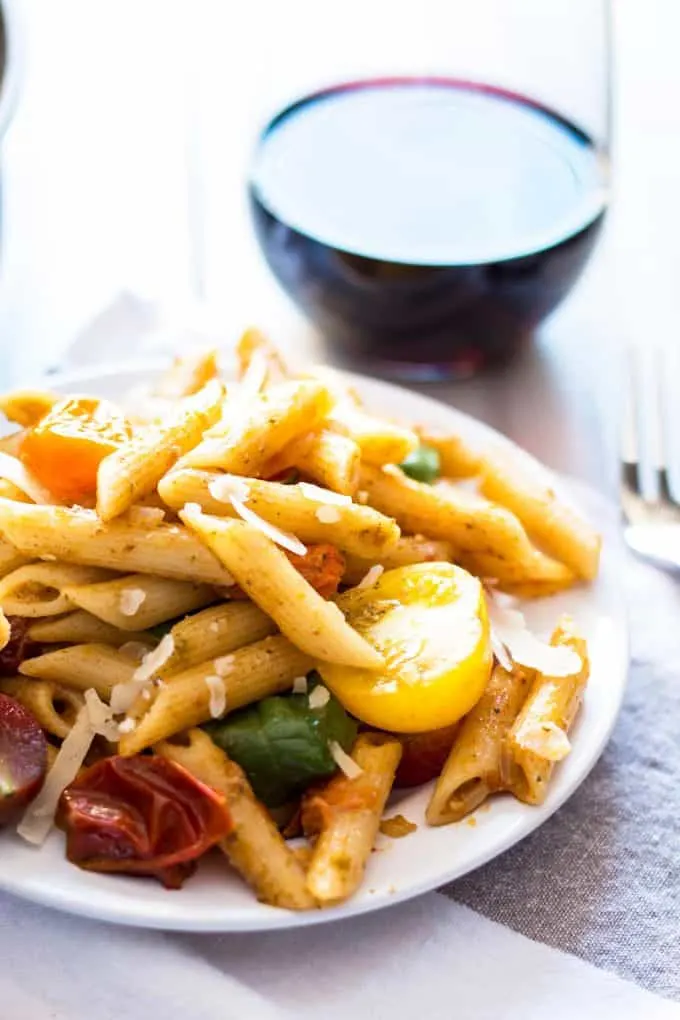 tomato and pesto pasta on a white plate with a glass of red wine