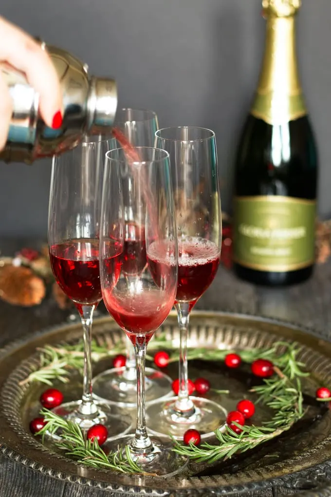 pouring cranberry juice and vanilla vodka into champagne flutes