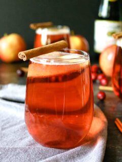 one cranberry apple cider mimosa with a cinnamon stick garnish
