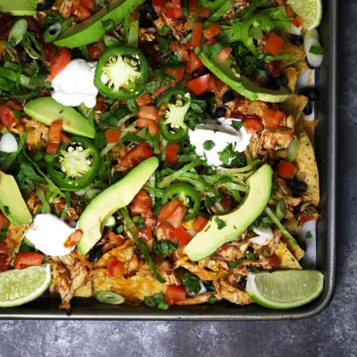 These sheet pan loaded chicken nachos are delicious AND easy to make! Make the slow cooker chicken the night before or the morning of to save time. This appetizer is the perfect game day food and it's also great for large holiday gatherings