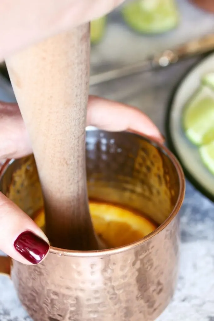 muddling an orange slice in a copper mug