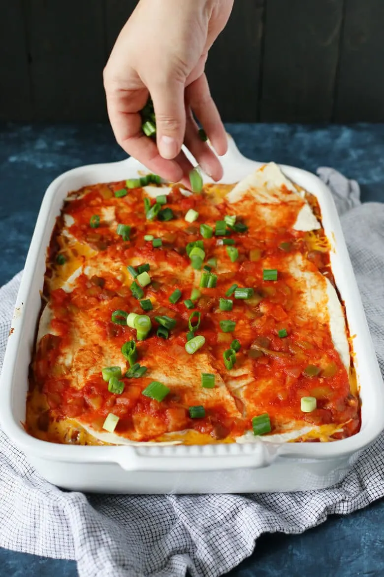 Cooked bean burrito casserole being garnished with green onions