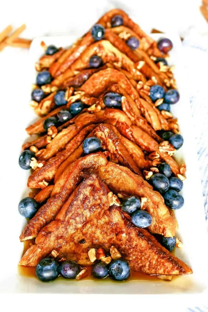 plate of cinnamon French toast topped with nuts, blueberries and syrup