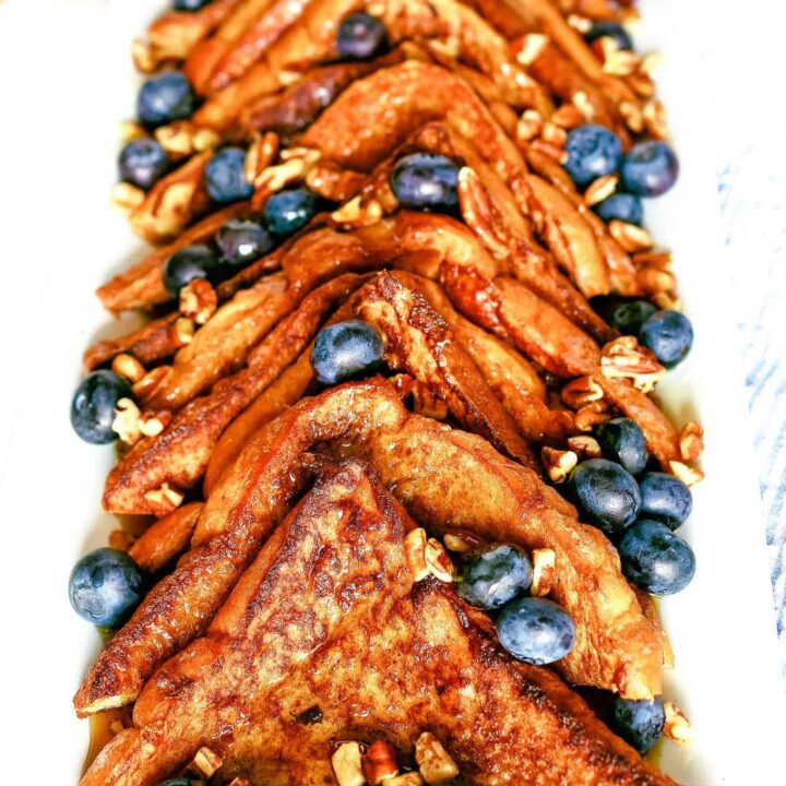 plate of cinnamon French toast topped with nuts, blueberries and syrup