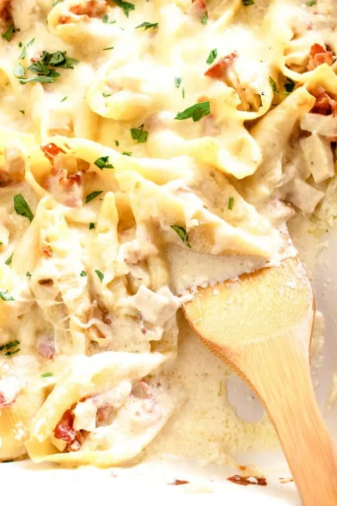 wooden spatula in a casserole dish full of chicken bacon Alfredo stuffed shells