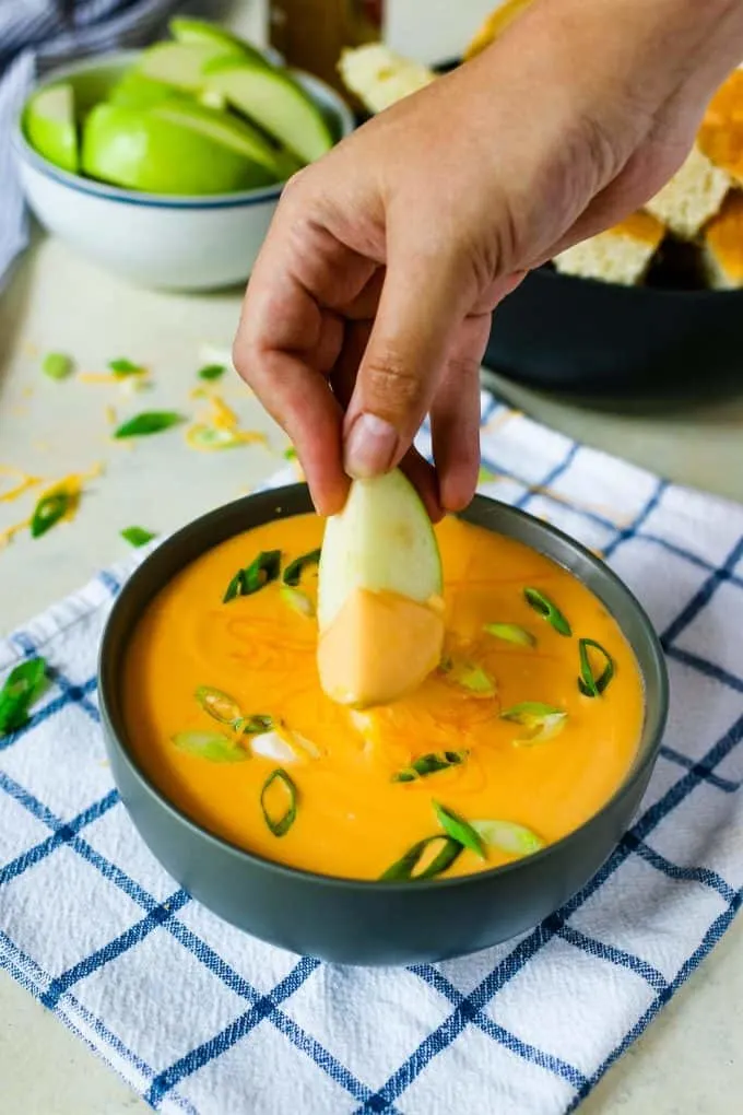 green apple being dipped into beer cheese dip