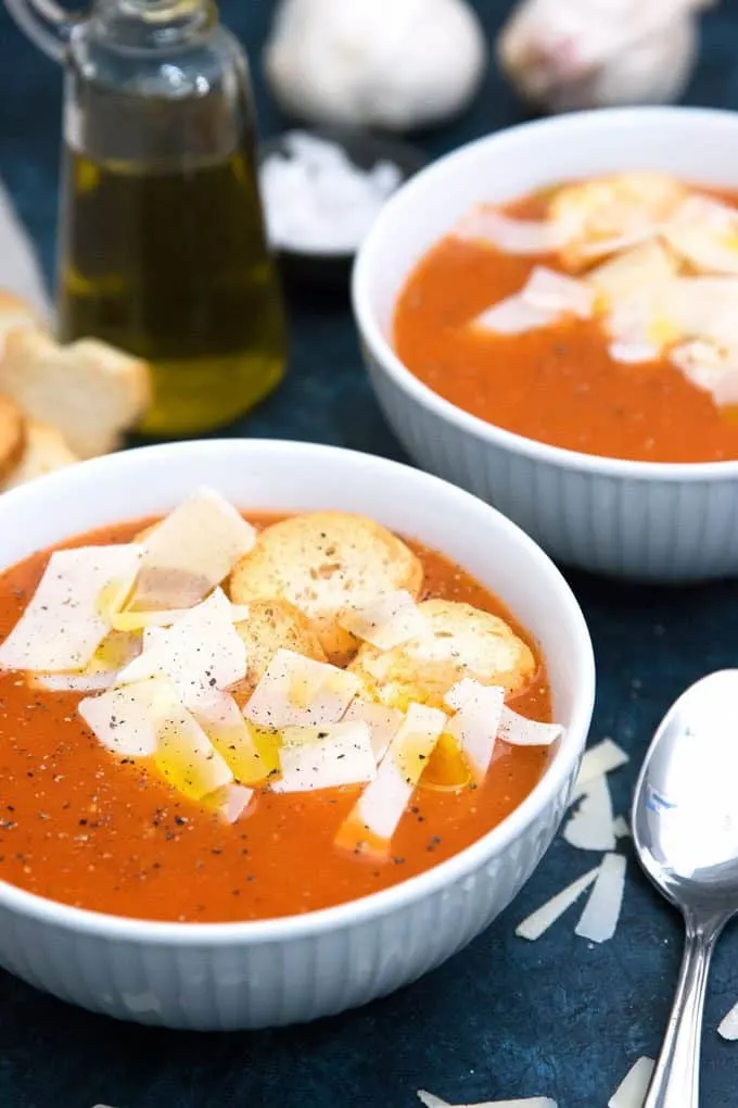 two bowls of roasted garlic tomato soup with croutons and parmesan cheese