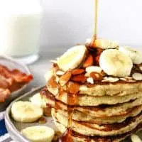 plate of almond banana pancakes with syrup being poured over fresh banana