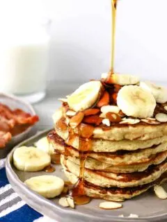 plate of almond banana pancakes with syrup being poured over fresh banana