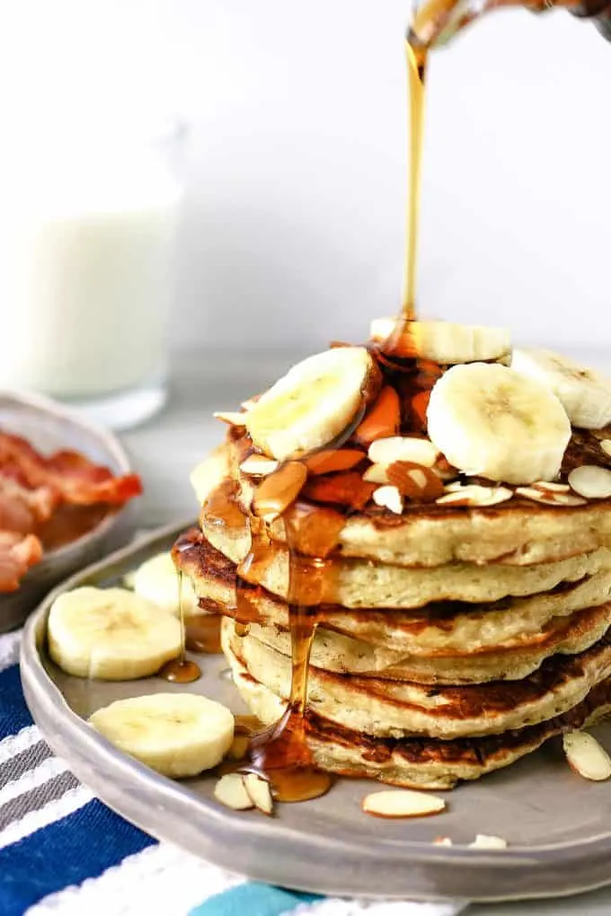 plate of almond banana pancakes with syrup being poured over fresh banana