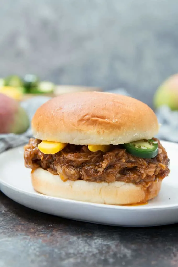 mango pulled pork in between a bun topped with mango and jalapeno slices