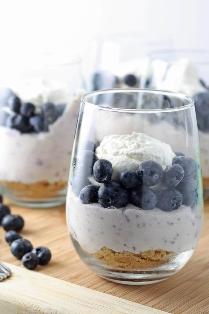 no bake blueberry cheesecake in a wine glass topped with whipped cream and blueberries
