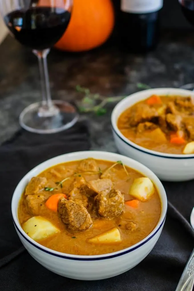 white bowl of pumpkin beef stew and a glass of red wine