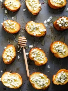 several blue cheese honey crostini on a sheet pan with a a honey stick