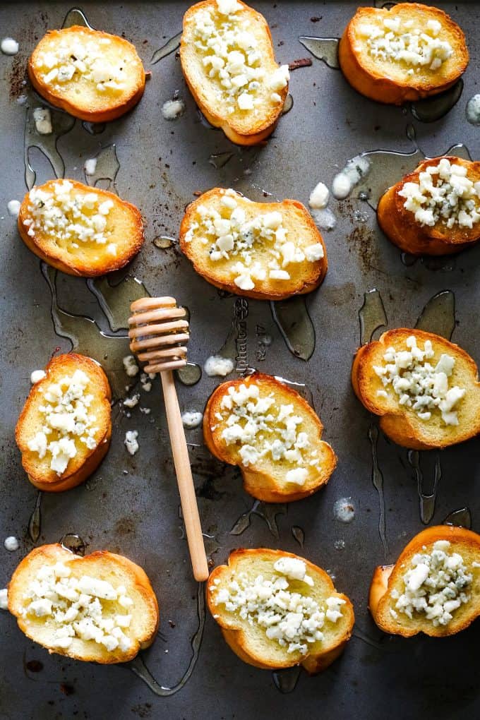 several blue cheese honey crostini on a sheet pan with a a honey stick