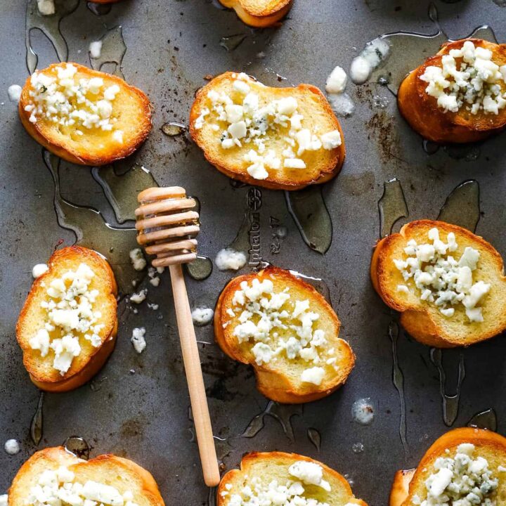 several blue cheese honey crostini on a sheet pan with a a honey stick