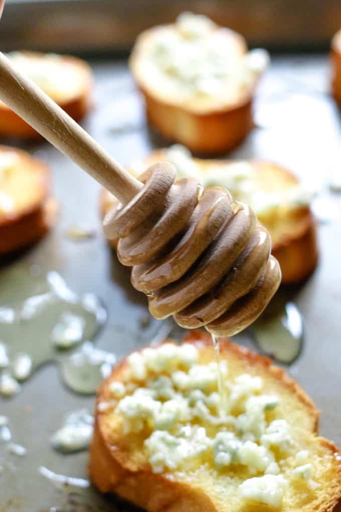 honey being sprinkled on a crostini topped with blue cheese