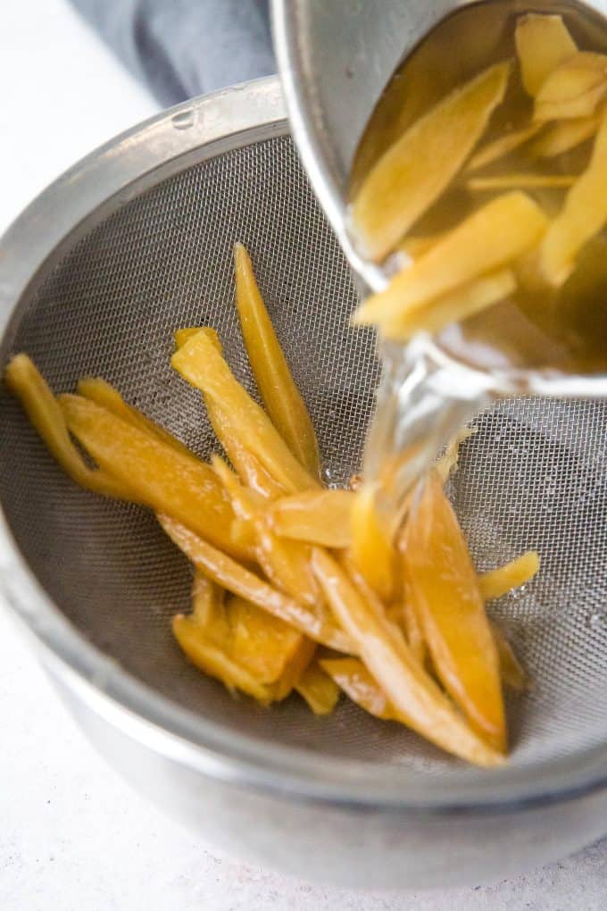 straining softened, cooked ginger over a colander and bowl