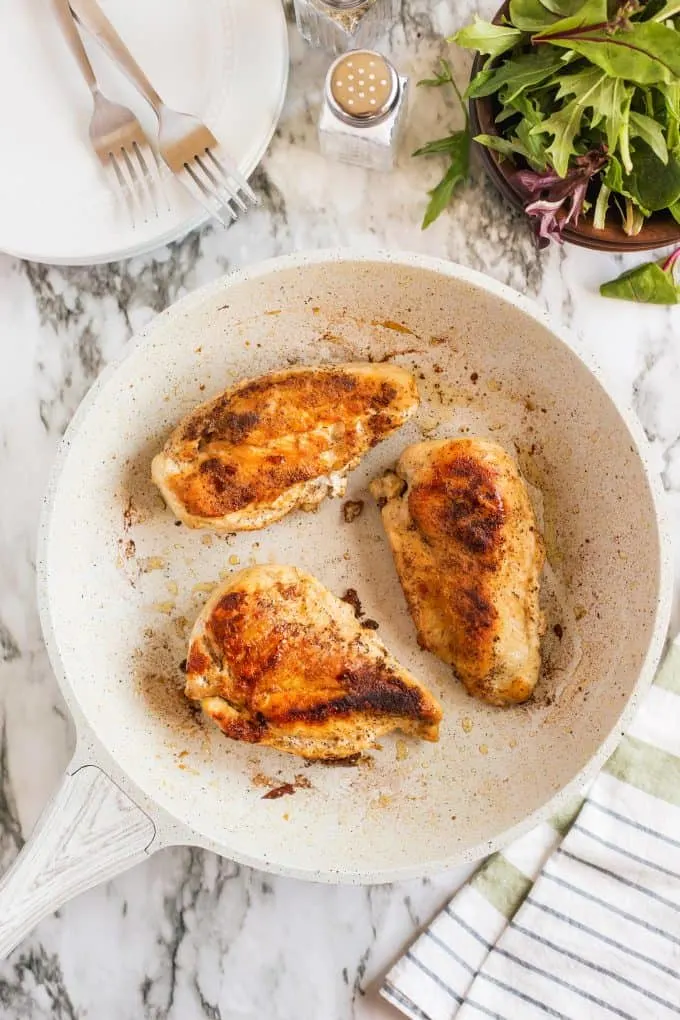three cooked chicken breasts in a pan on a marble backdrop