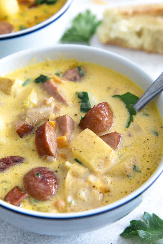 white bowl full of potato kielbasa soup, with a spoon. The sausage is crispy and the soup is garnished with fresh parsley
