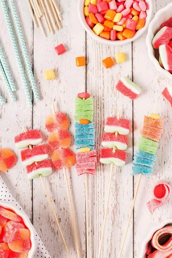kandy kabobs on a wooden table with bowls of gummy candy surrounding them