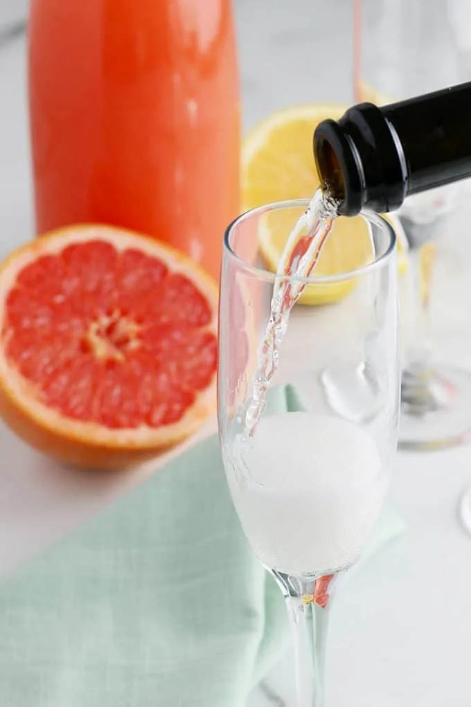pouring champagne into a glass with a half grapefruit in the background