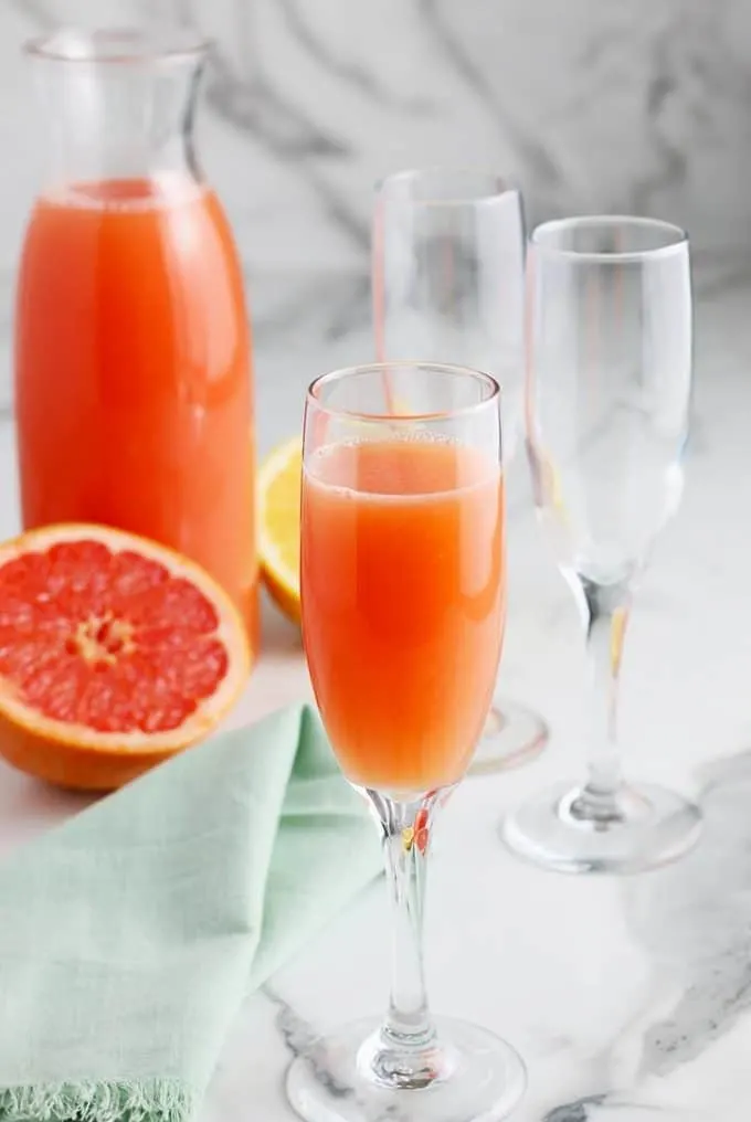 carafe of grapefruit juice, two empty champagne flutes and one grapefruit mimosa