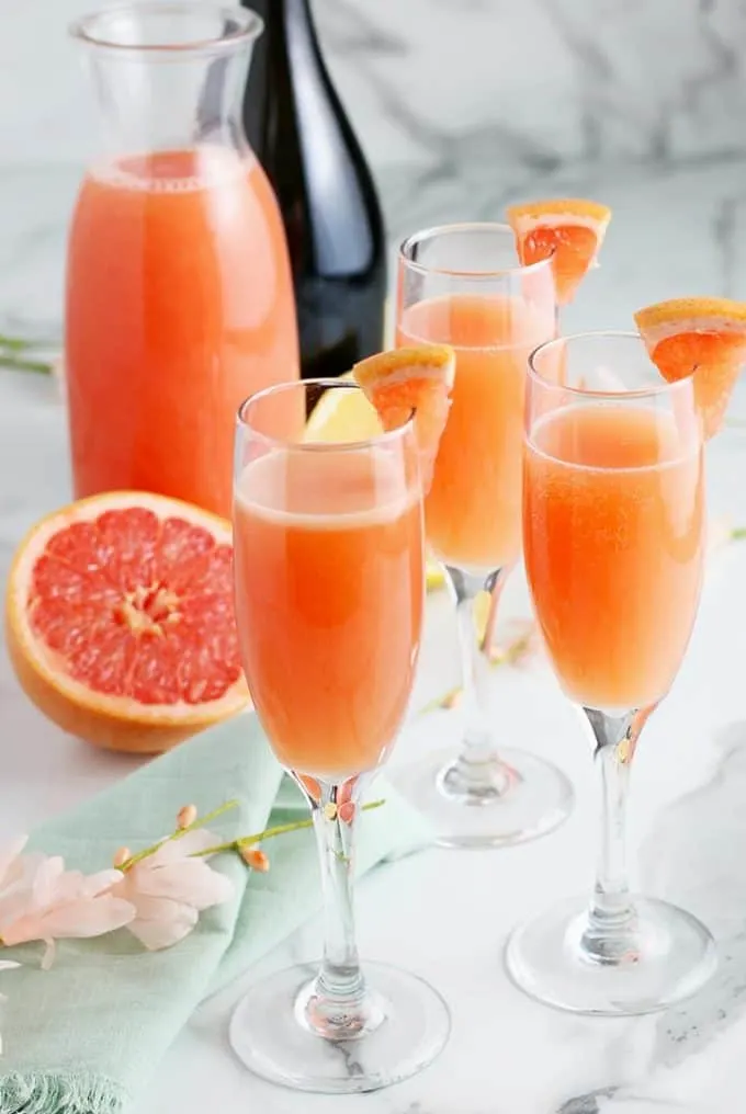 3 grapefruit mimosas in champagne flutes on a marble table