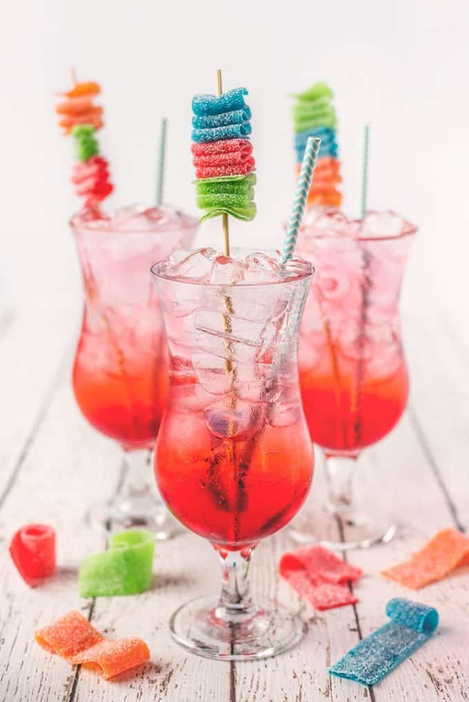 3 shirley temple drinks in tall glasses on a white wooden table garnished with candy kabobs
