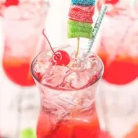 shirley temple garnished with a maraschino cherry, blue straw, and multicolored candy skewer
