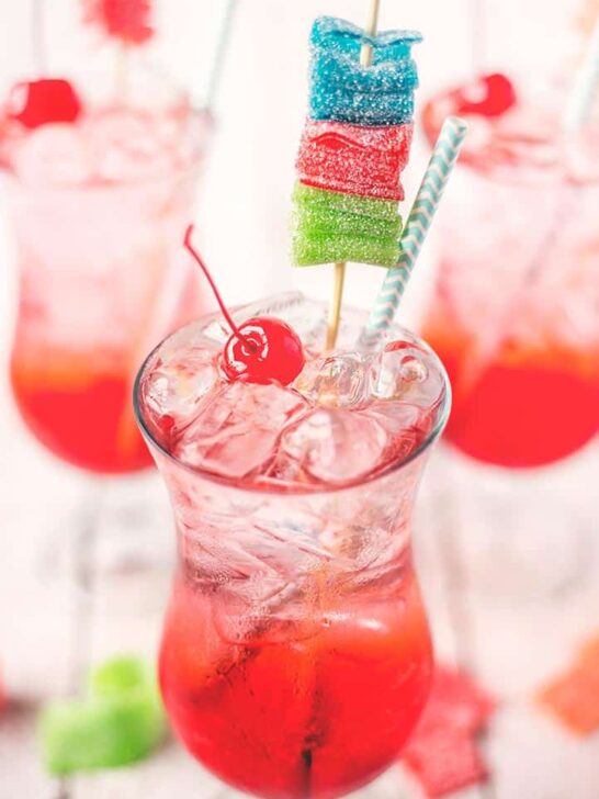 shirley temple garnished with a maraschino cherry, blue straw, and multicolored candy skewer