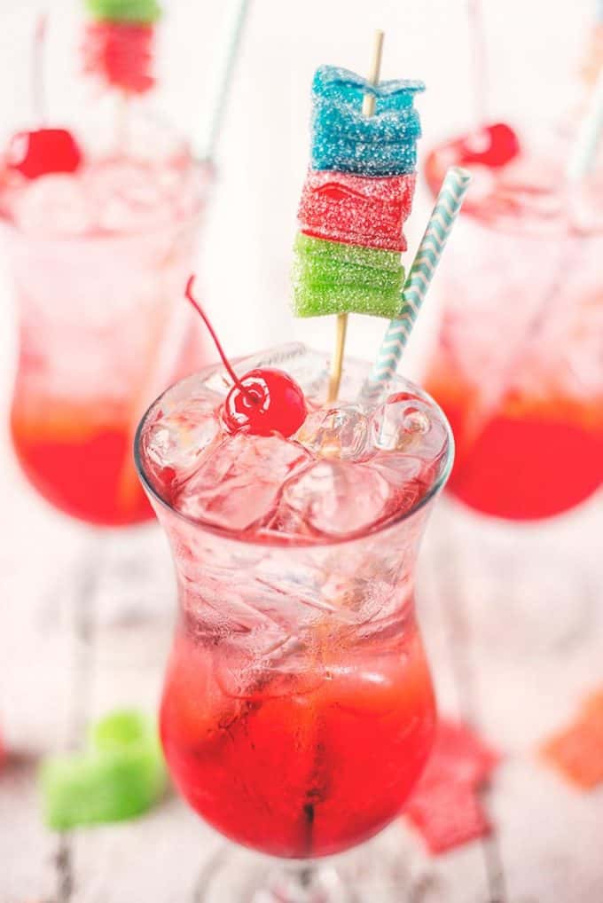 shirley temple garnished with a maraschino cherry, blue straw, and multicolored candy skewer