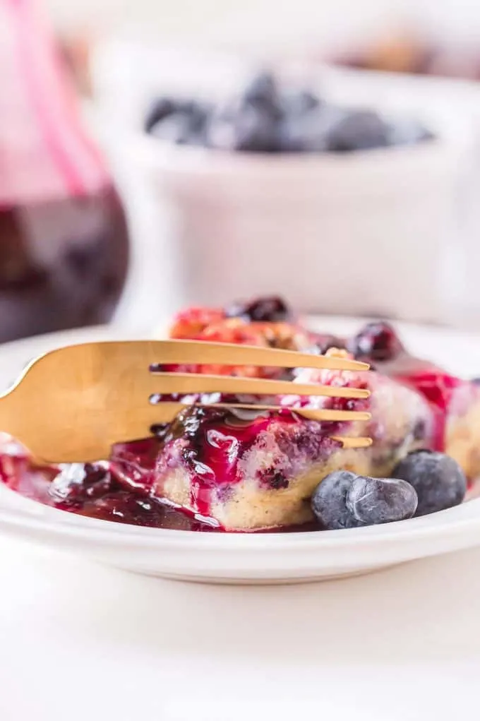 a gold fork breaking away a small piece f French toast casserole on a white plate