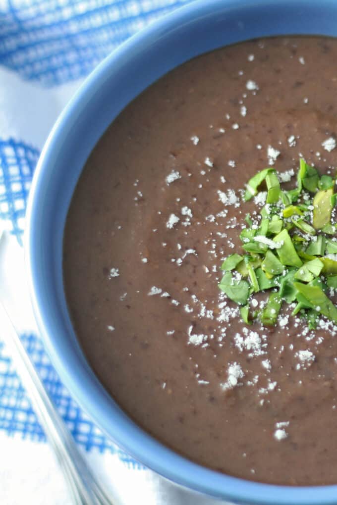 close up shot of black bean soup with cheese and chives in a blue bowl on a blue napkin