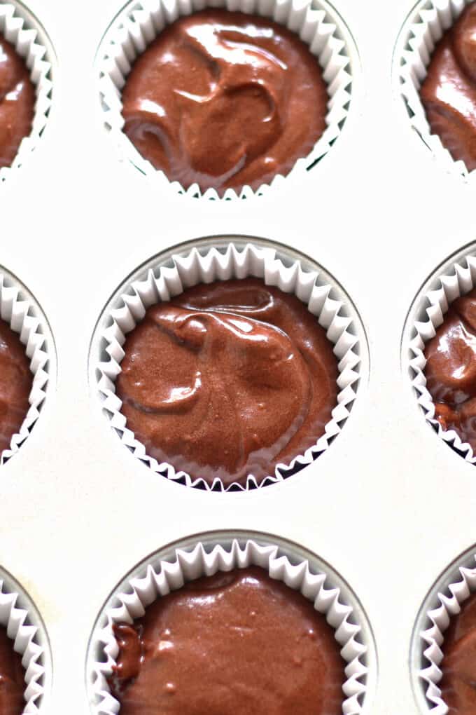 chocolate cupcake batter in a silver muffin/cupcake tray with white cupcake liners