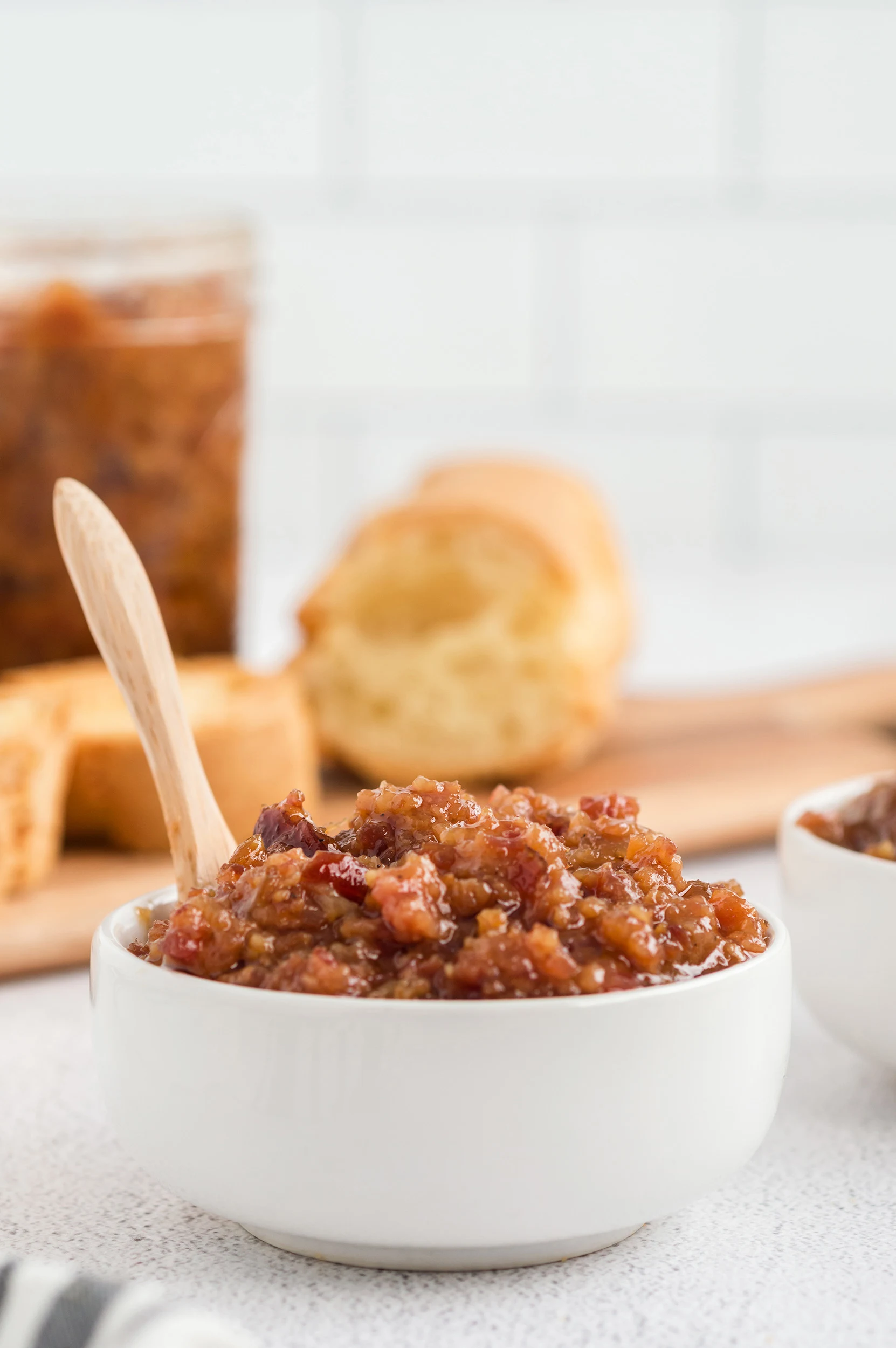 straight on photo of a white bowl of bacon jam with a wooden spoon inside