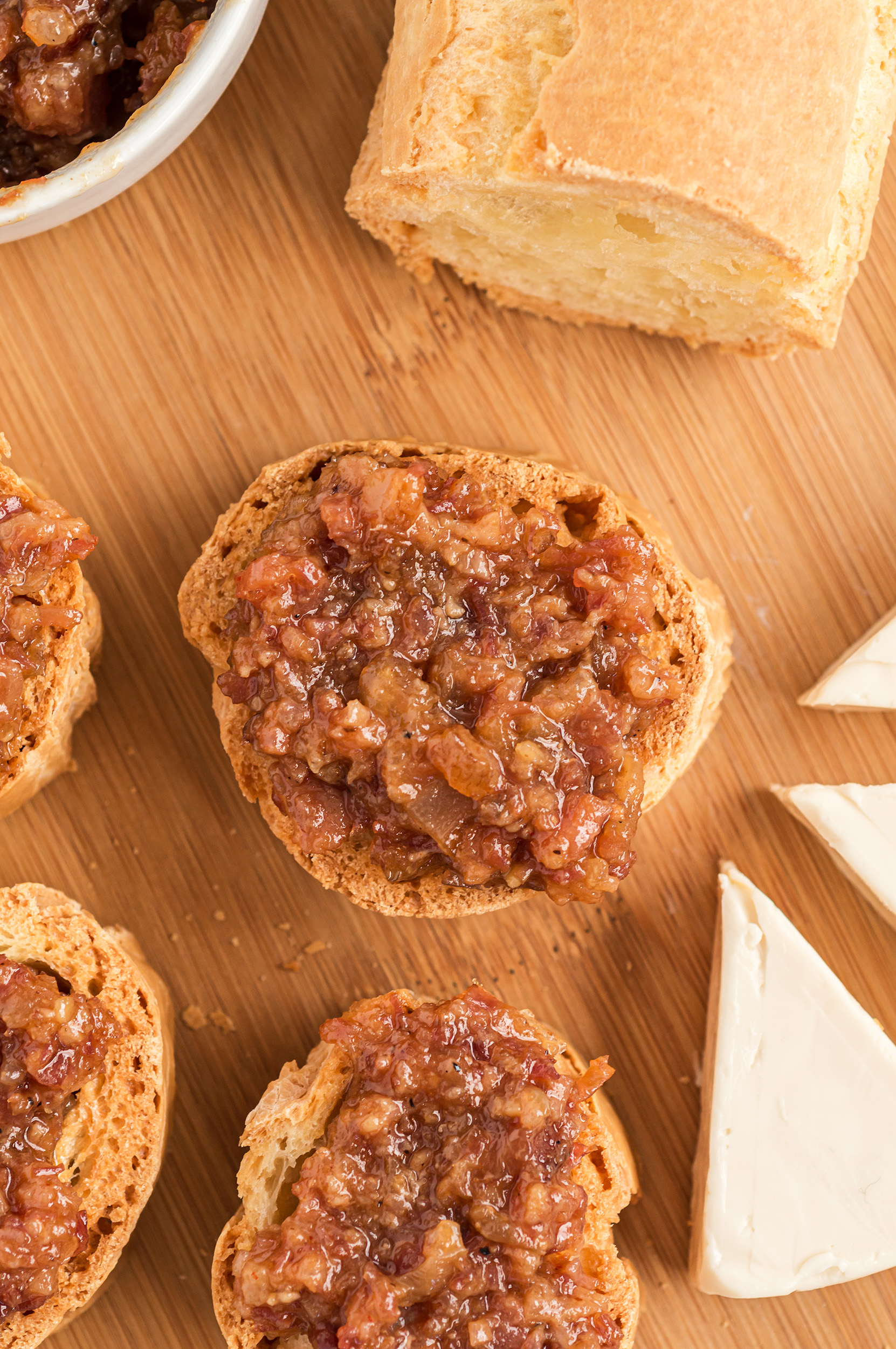 several bacon-jam topped crostini with unsliced bread and cheese wedges